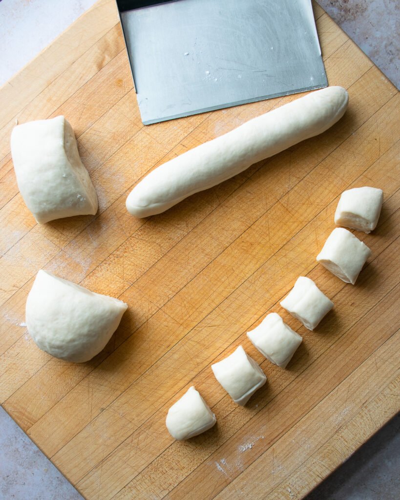 Pierogi dough divided into portions on a cutting board with a bench scraper.