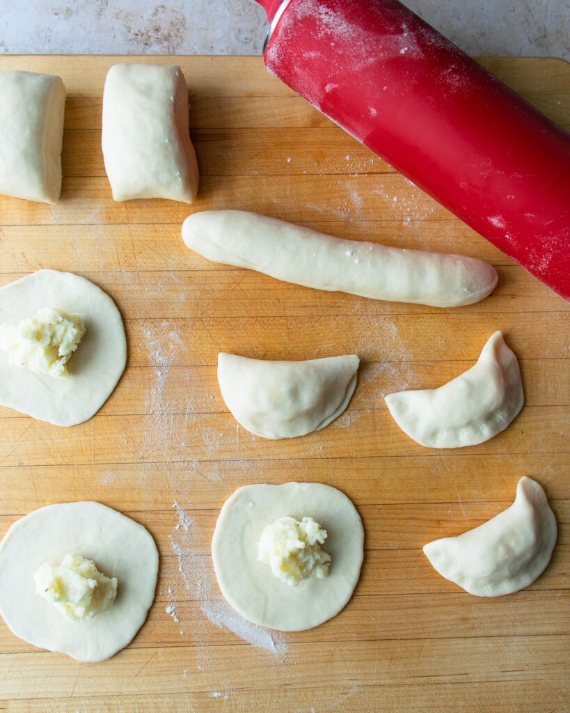 Pierogies in the making - some finished, some just dough with filling - and a red rolling pin.