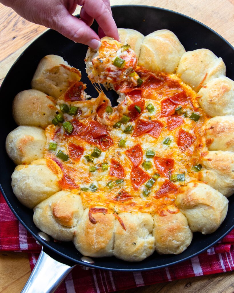 Fingers pulling a ball of dough out of a skillet full of pizza dip.