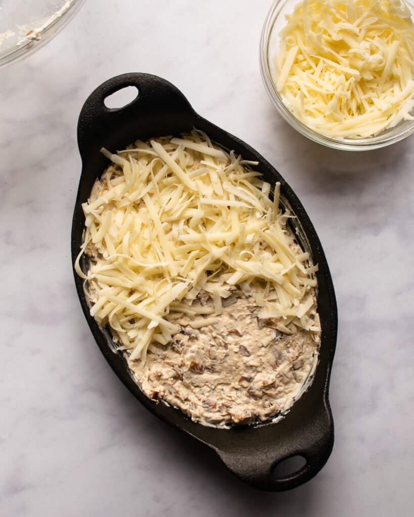 A cast iron gratin dish with warm french onion dip inside and Gruyère cheese on top.