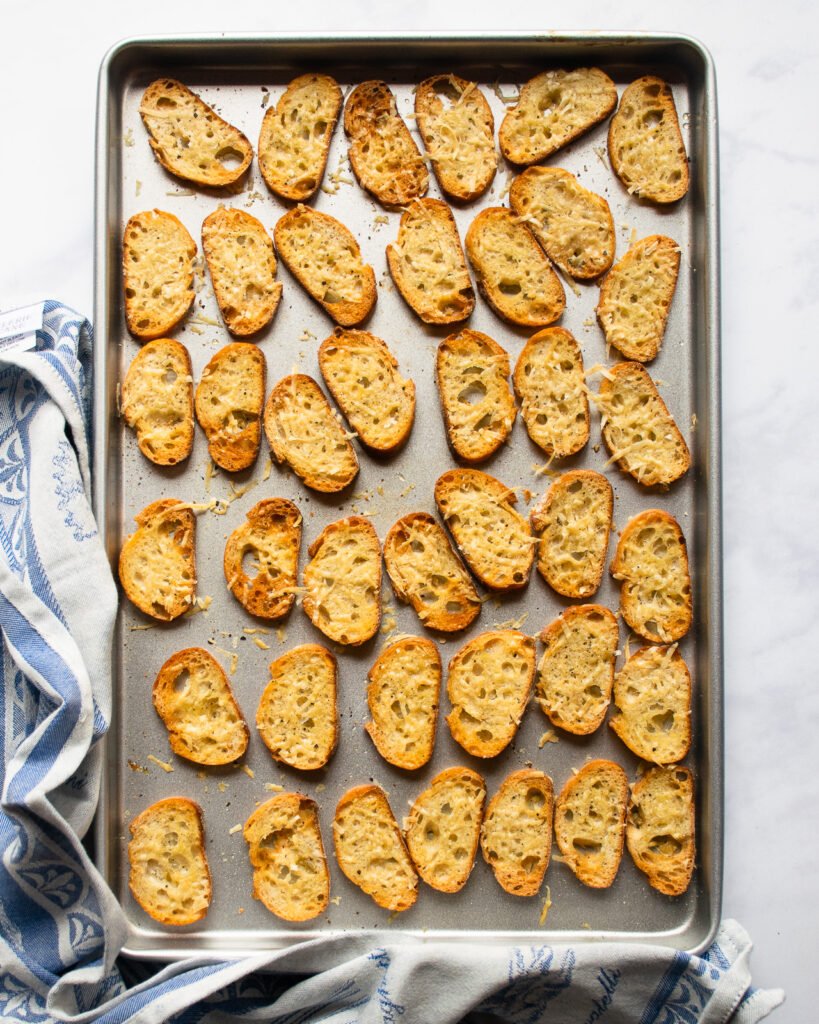 Crostini on  a sheet pan with a blue towel wrapped around the bottom edge.