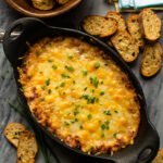 Warm French Onion Dip in a cast iron gratin dish with parmesan crostini around.