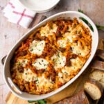 Ziti al Forno in a white oval casserole on a countertop with sliced bread and a stack of bowls next to it.