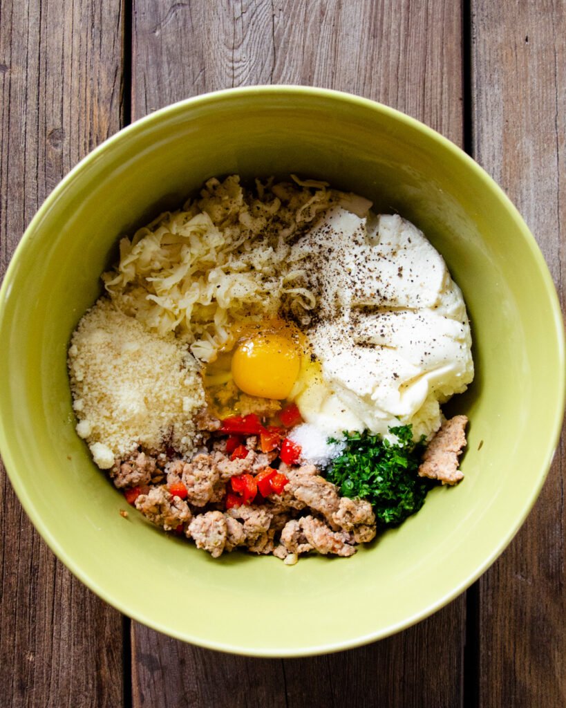 Ingredients in a bowl - ground turkey, red pepper, mozzarella cheese, parmesan cheese, parsley, egg, ricotta cheese.