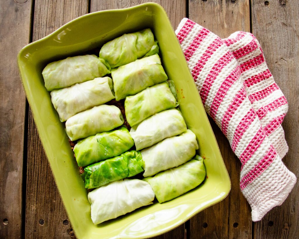 Cabbage Stuffed Shells in a green casserole dish with a pink and white striped towel.