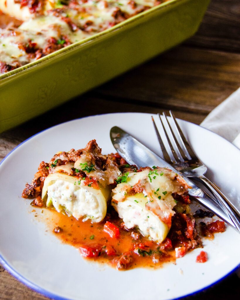 A portion of ricotta stuffed cabbage shells on a white plate with blue rim and a knife and fork.
