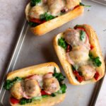 Three Italian Chicken Meatball Grinders on a baking sheet.