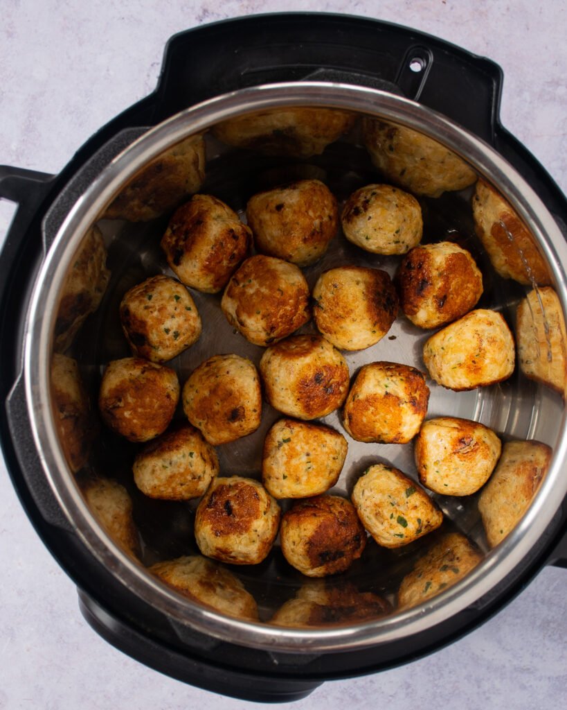 Meatballs browning in a pressure cooker.
