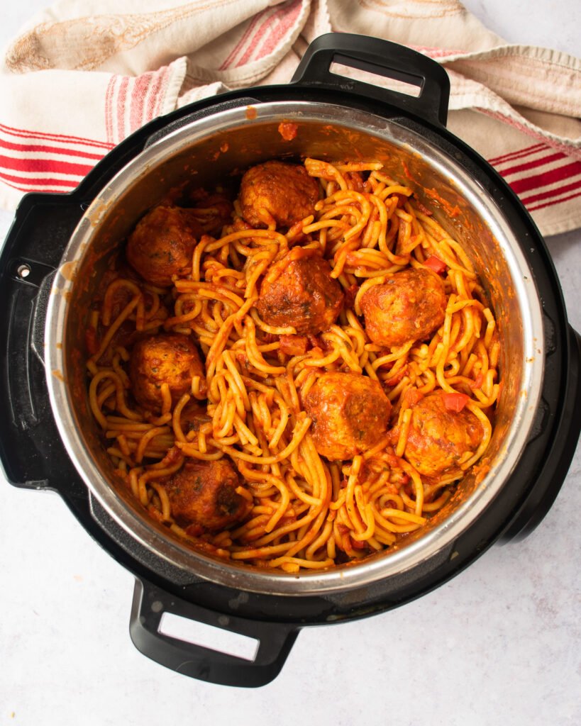 Spaghetti and meatballs in a pressure cooker with a red and tan towel near by.