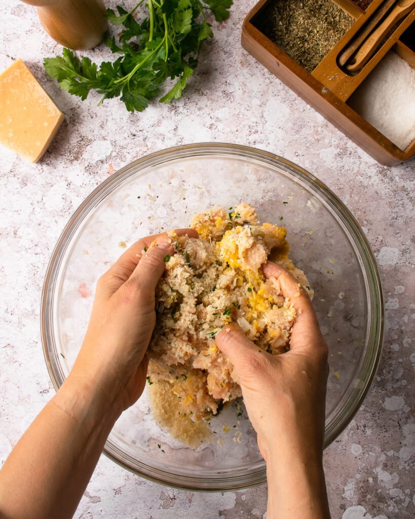 Hands mixing ingredients together in a glass bowl.