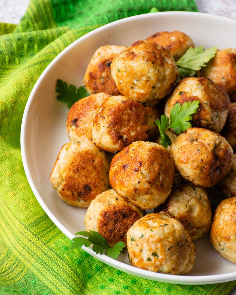 A white bowl of Italian chicken meatballs surrounded with a green napkin.