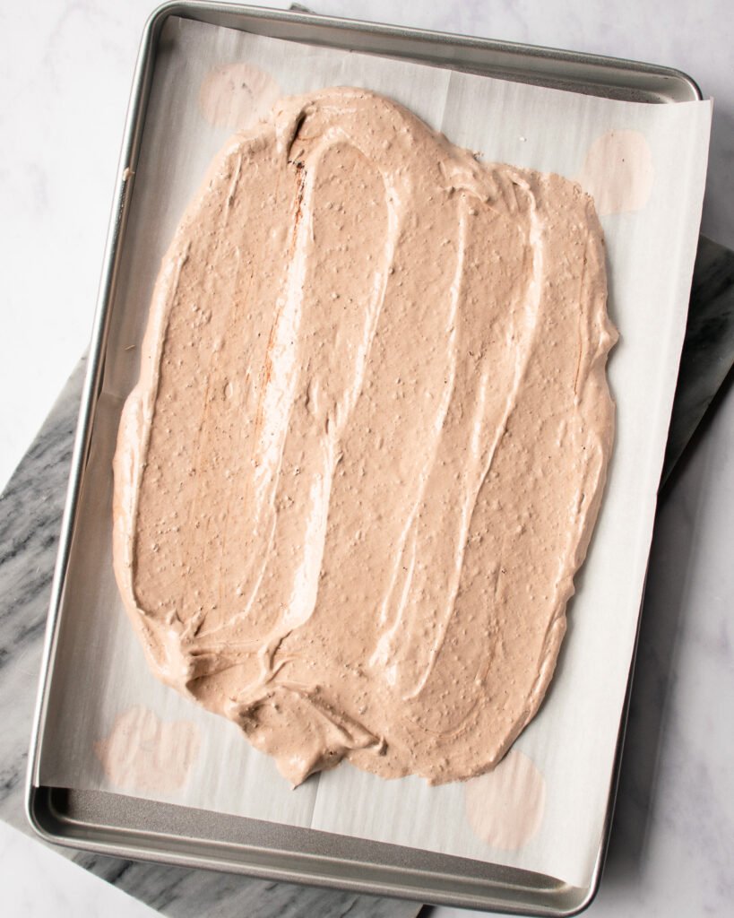 Raw meringue spread on a parchment paper-lined baking sheet.