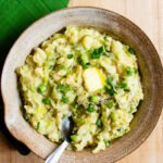 A ceramic bowl full of colcannon with a spoon sticking out of it and a pat of butter melting on top.