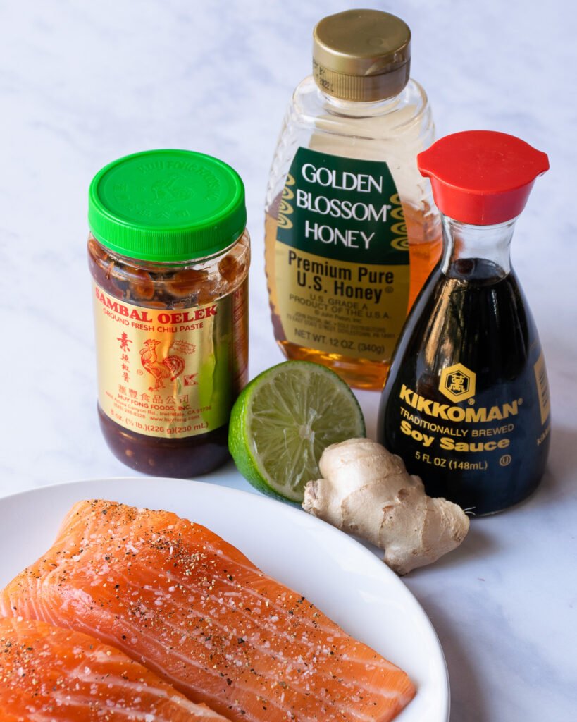 Ingredients for honey soy salmon - chili garlic paste, soy sauce, garlic, lime juice and honey - in front of a plate of salmon.