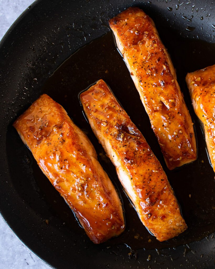 Salmon fillets in a non-stick skillet with a glaze on them.