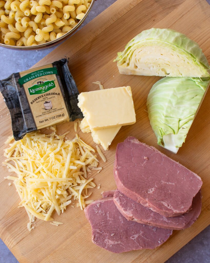 Ingredients on a wooden cutting board - corned beef, cheese, cabbage and pasta.