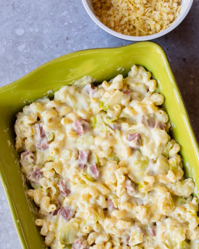 Irish Cheddar Mac and Cheese in a green casserole dish with a bowl of breadcrumbs next to it.
