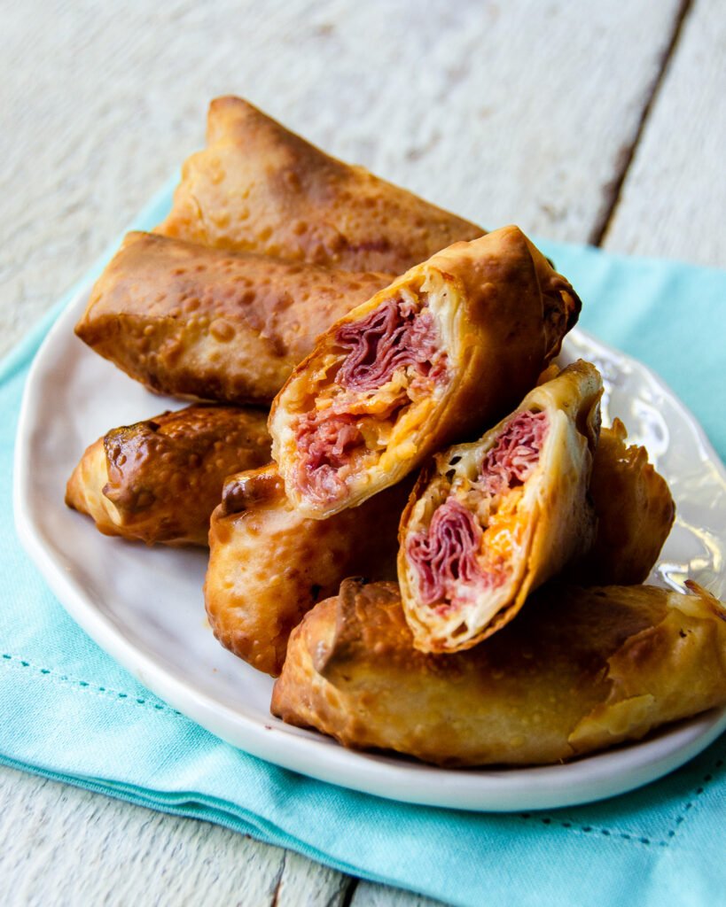 Reuben Egg Rolls on an oval white plate with a turquoise napkin underneaath.