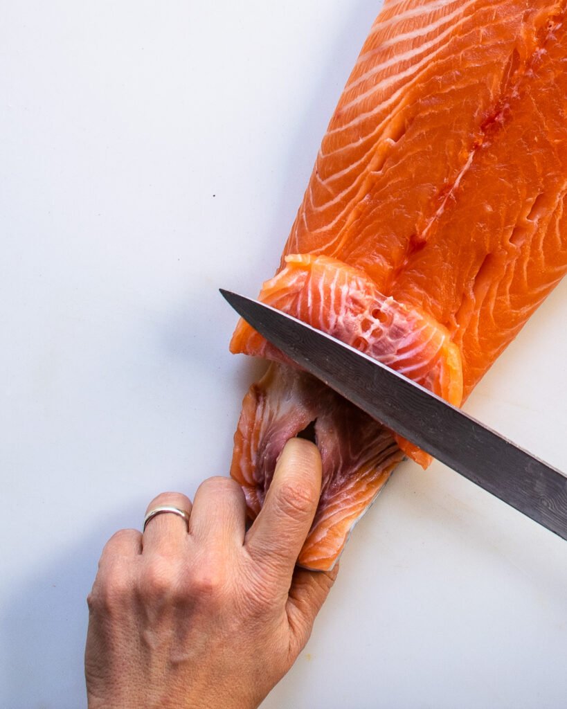 A hand holding onto the skin of salmon through a hole in the skin, while a knife holds the flesh of the salmon up.