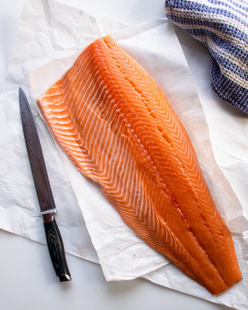 A side of salmon on paper with a long carving knife beside it.