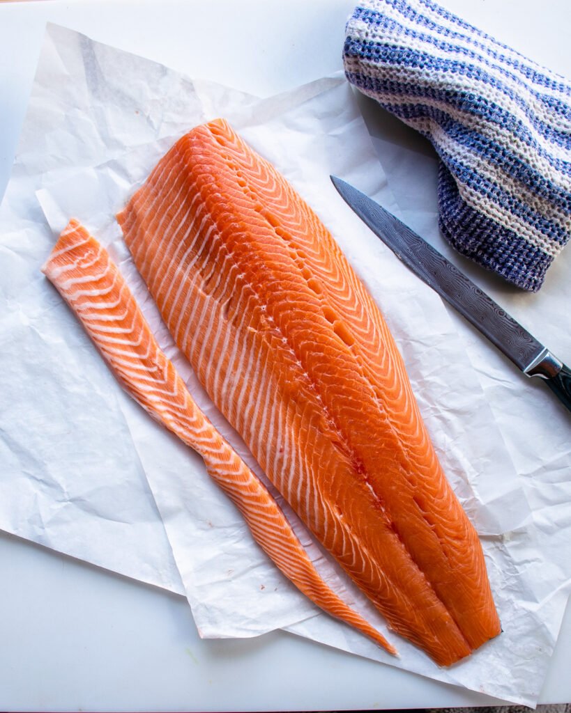 A side of salmon with the belly fat cut away from the rest of the fish, a knife and towel next to it.