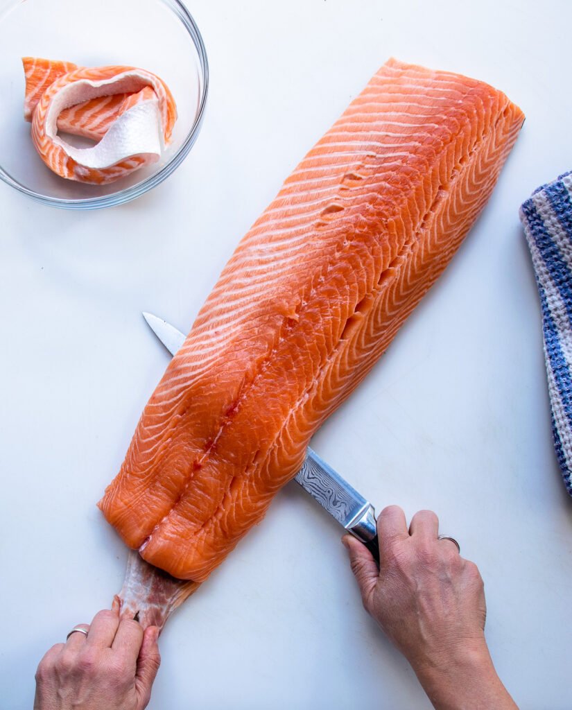 Removing the skin from a side of salmon on a white board.
