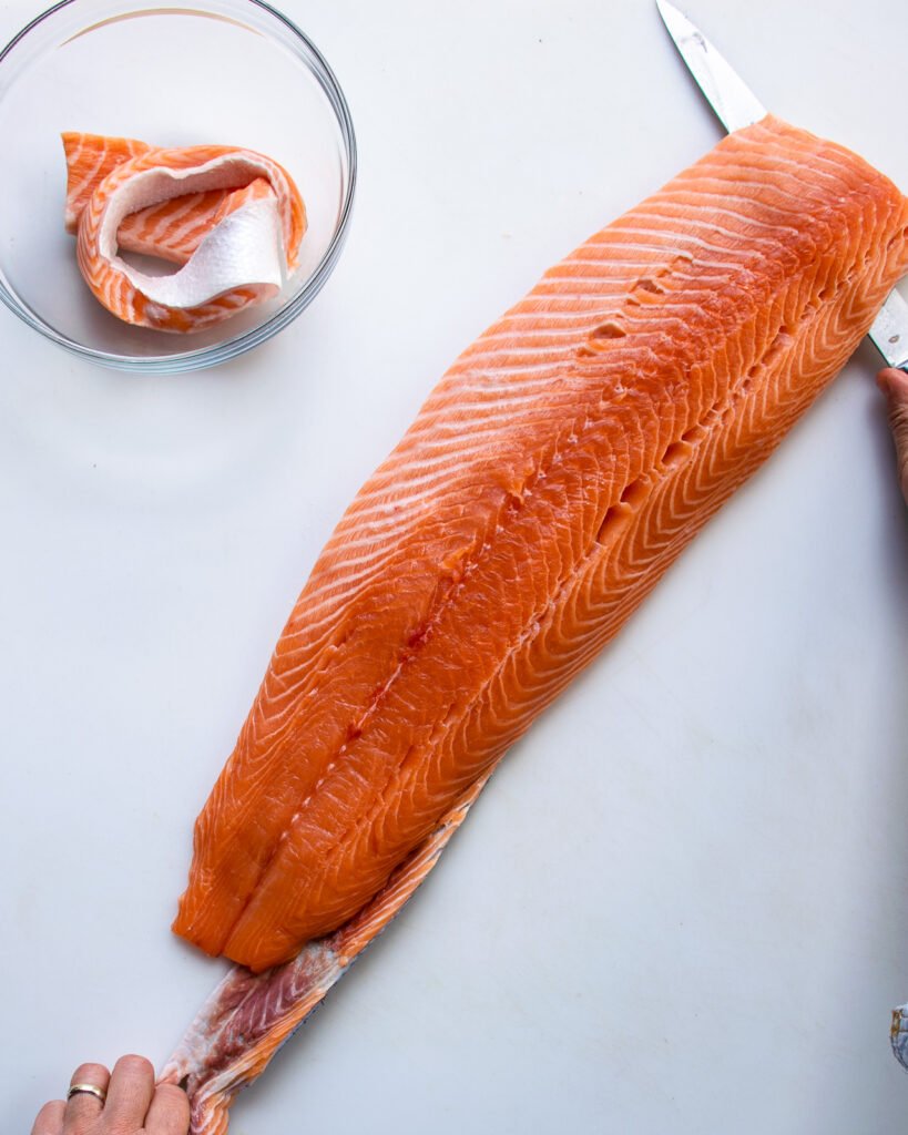 A knife skinning a side of salmon on a white board.