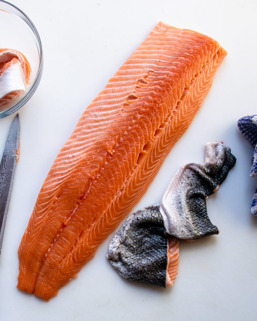 A side of salmon with the skin next to it on a white board.
