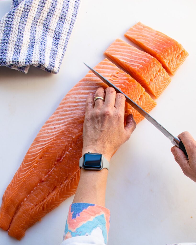 Two hands cutting a side of salmon into fillets.