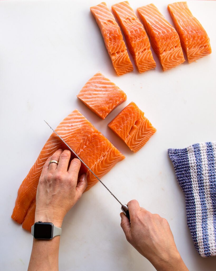 Two hands cutting a side of salmon into different shaped fillets.