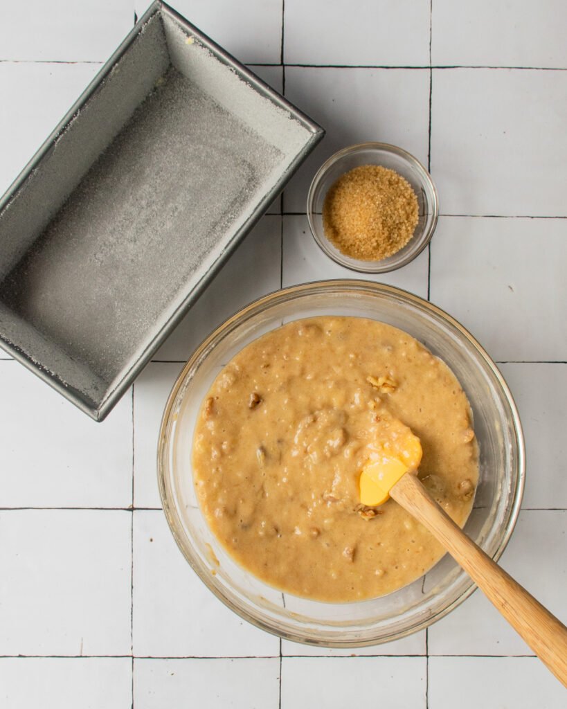 Batter in a bowl with a spatula next to a loaf pan.