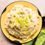 Cheddar Garlic Smashed Potatoes in a rustic yellow bowl with a light green plaid napkin and spoon.