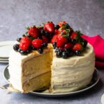 Vanilla Layer cake with berries and buttercream frosting on a plate with a slice being taken out.