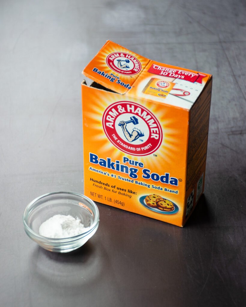 A box of baking soda with a small dish of baking soda in front of it.