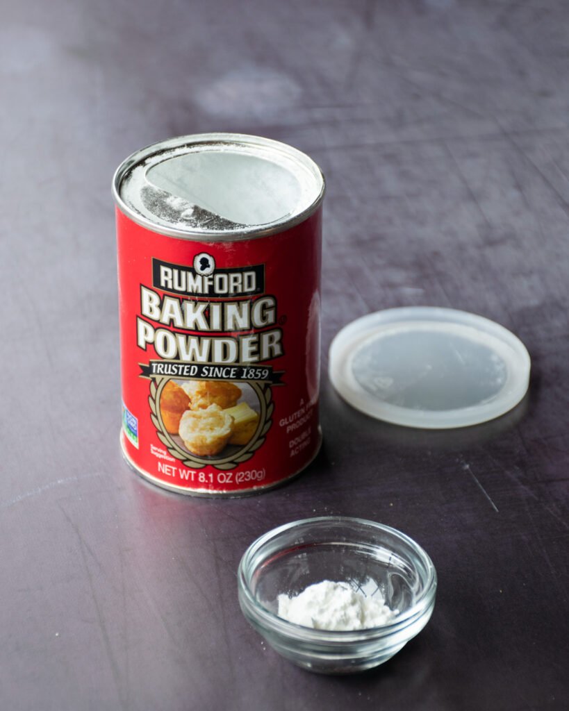 A can of baking powder with a small dish of baking powder in front of it.