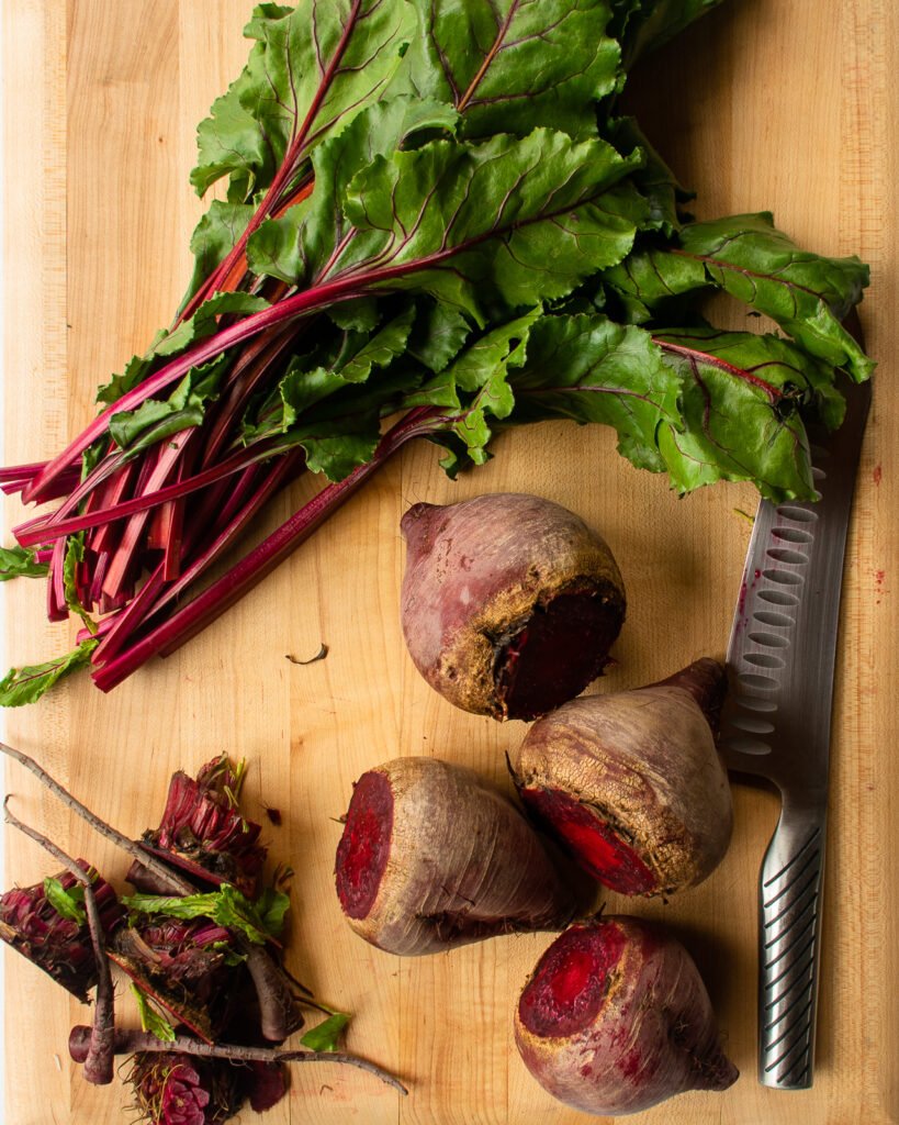 Beets trimmed on a cutting board with a knife.