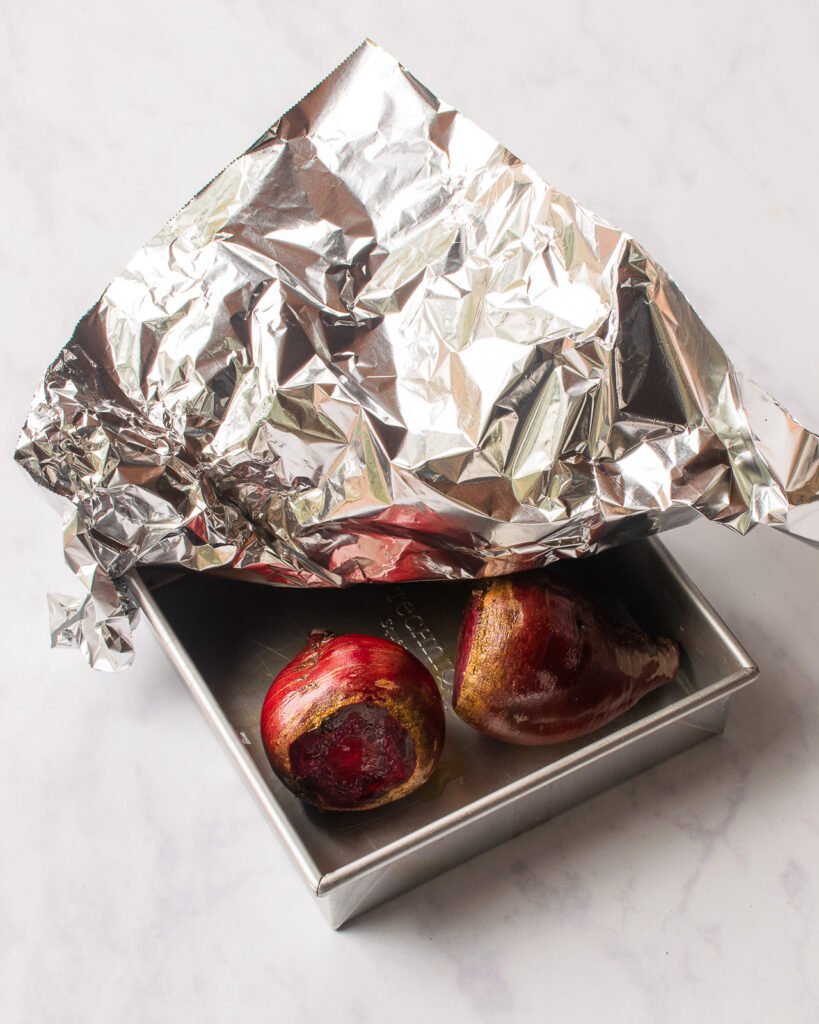 Beets in a square cake pan, partially covered with aluminum foil.