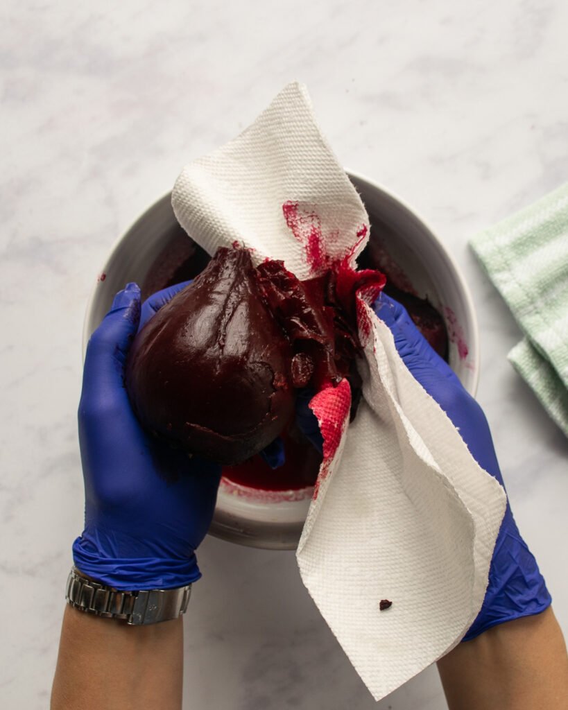 Two hands with latex gloves peeling beets with a piece of paper towel.