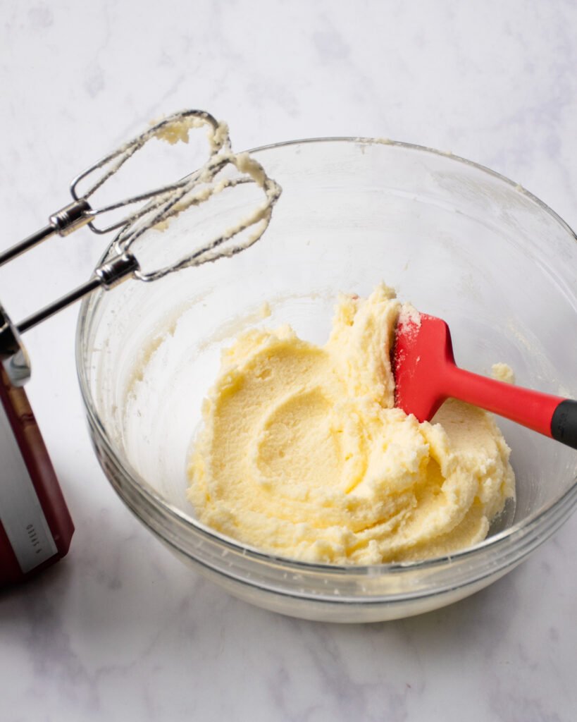 Perfectly creamed butter and sugar in a glass bowl with a red hand mixer next to it.
