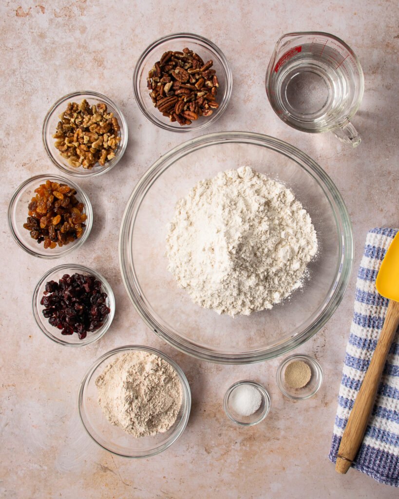 Ingredients in bowls - flour, salt, yeast, golden raisins, cranberries, pecans, walnuts and water.
