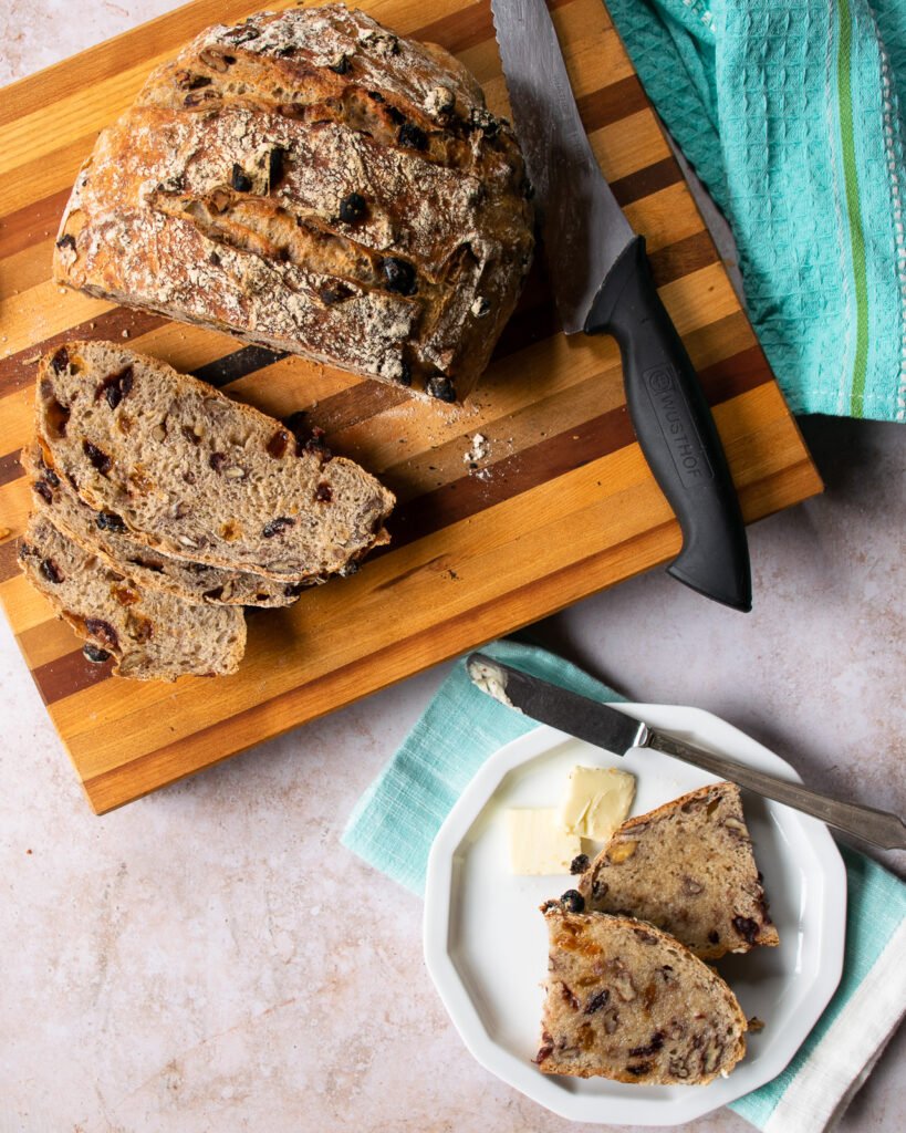 A plate with bread and butter next to a cutting board with a whole loaf and some slices.