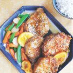 Orange glazed pork chops on platter with vegetables and ride in a bowl.