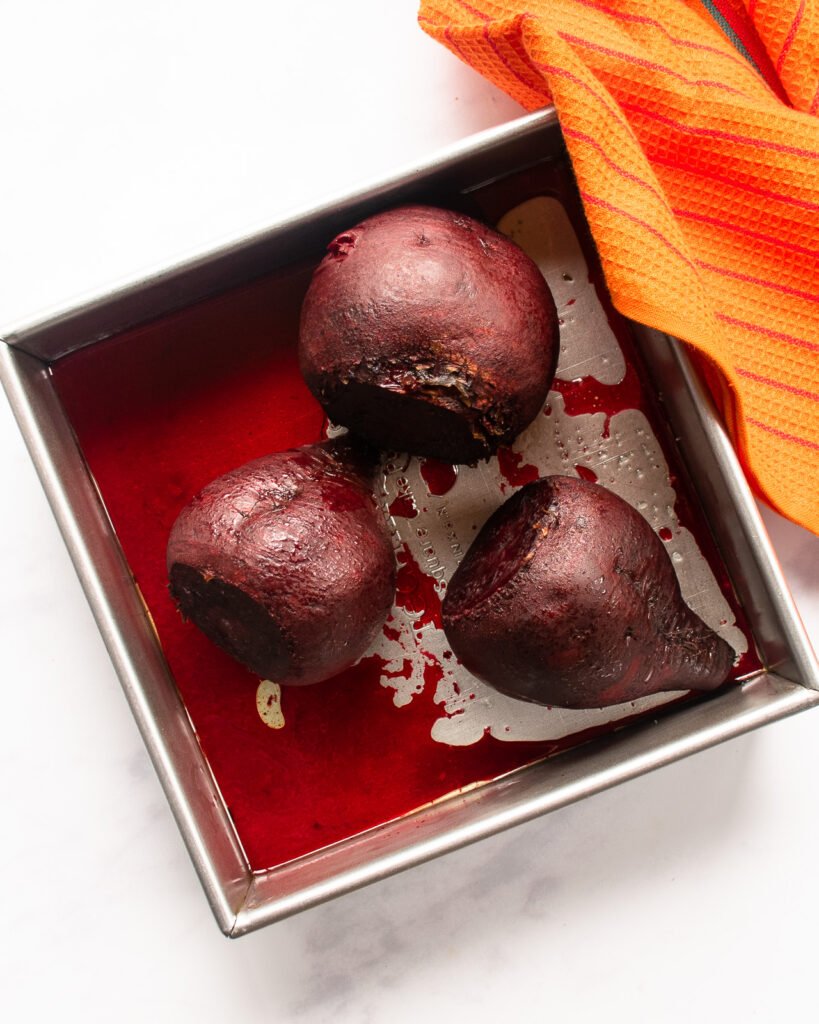 Beets cooked in a square cake pan with an orange towel on the side.