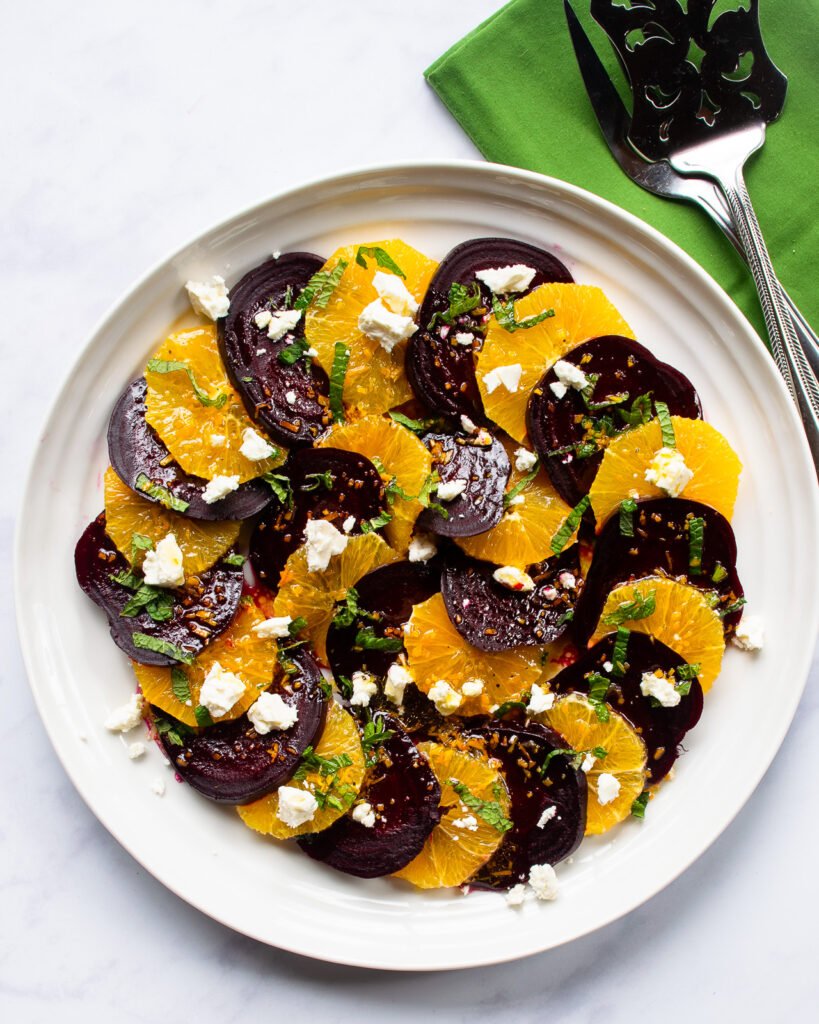 Beet and orange salad on a white plate with a green napkin on the side.