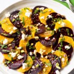 Orange and Beet salad on a white plate with a green napkin and server next to it