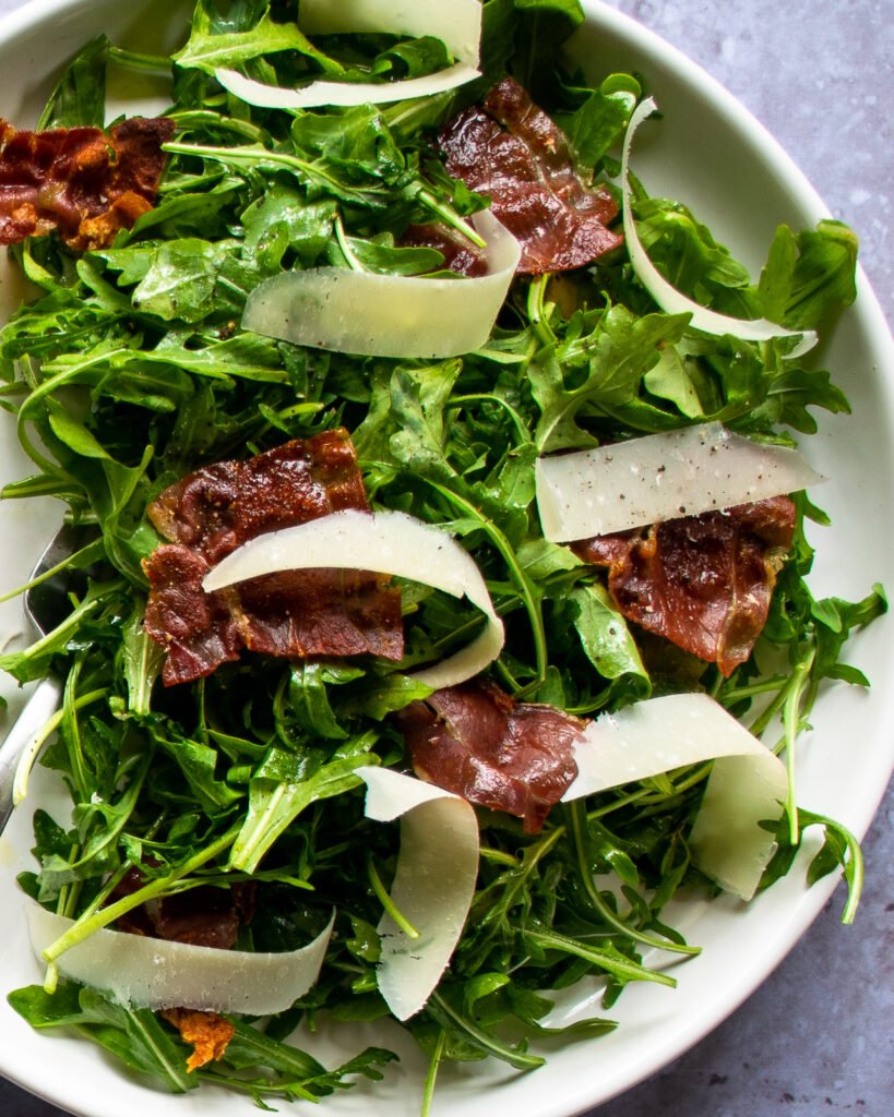 A close up shot of an arugula salad with parmesan and prosciutto