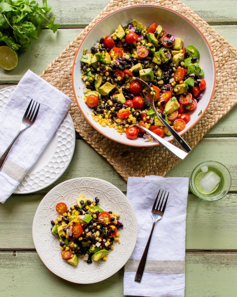 A plate of avocado tomato salad with a serving bowl of salad.