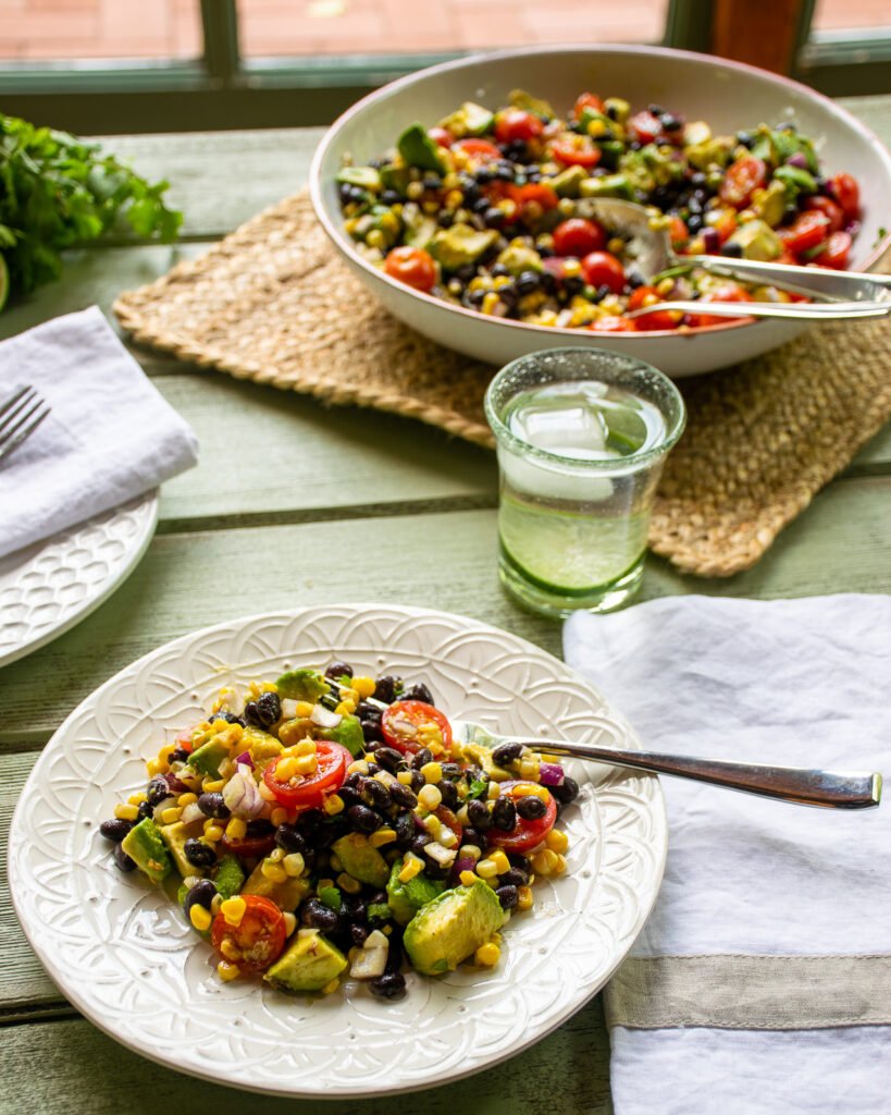 A serving of avocado tomato salad on a green table near a window.
