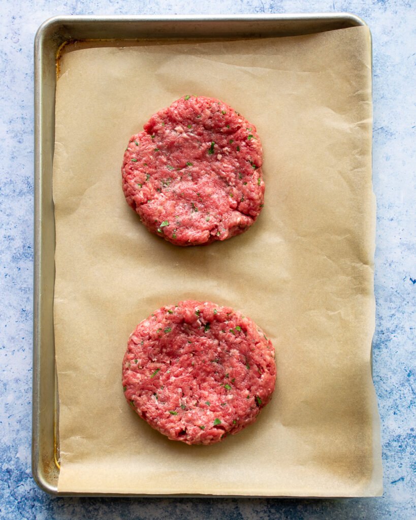 Two burger patties on brown parchment paper.