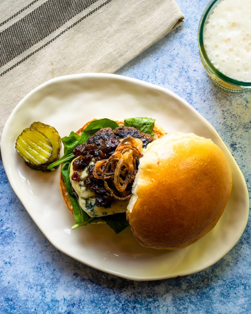 An assembled bacon blue burger on an oval white plate.